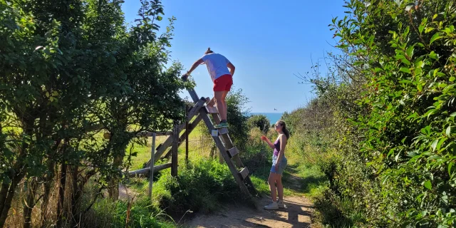 Une famille de randonneur, grimpe sur les passe-clôture du Sentier du Littoral entre Mers-les-Bains et Ault